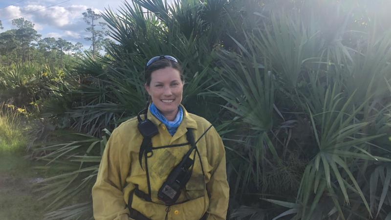 Park Ranger Sara Travis stands with native vegetation in fire gear before a burn 