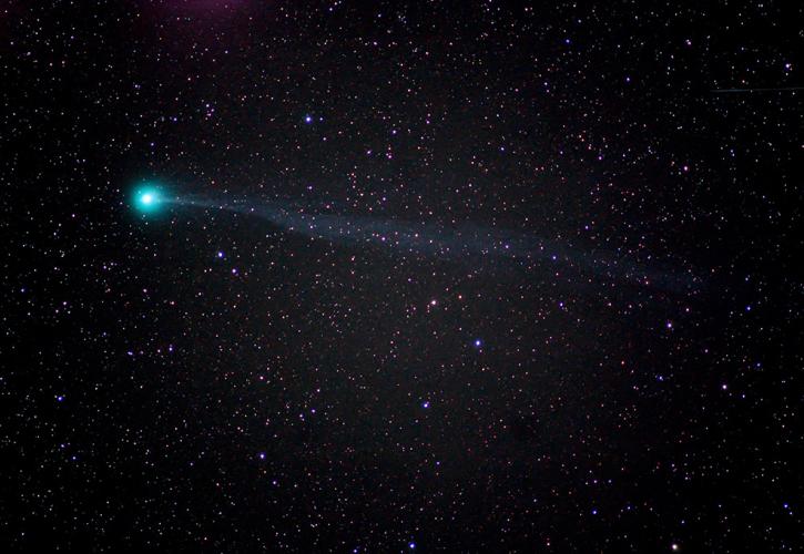 A bight blue comet flying across the night sky with stars surrounding it. 