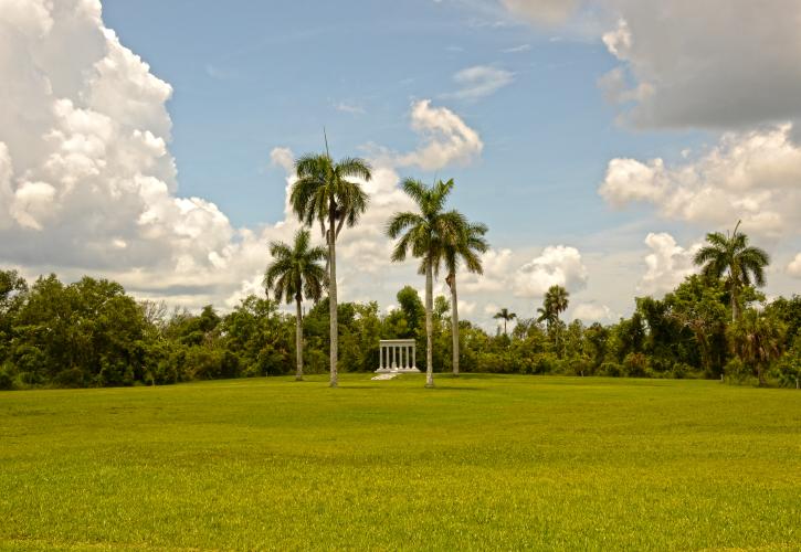 Open grassy field with puffy white clouds royal palms and memorial structure
