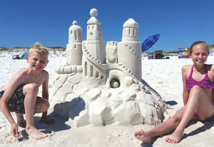 Kids smiling proud of the amazing sandcastle they built