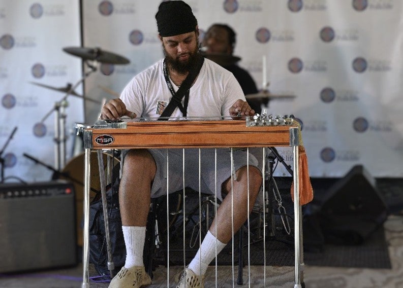 A bearded Black man playing a steel guitar