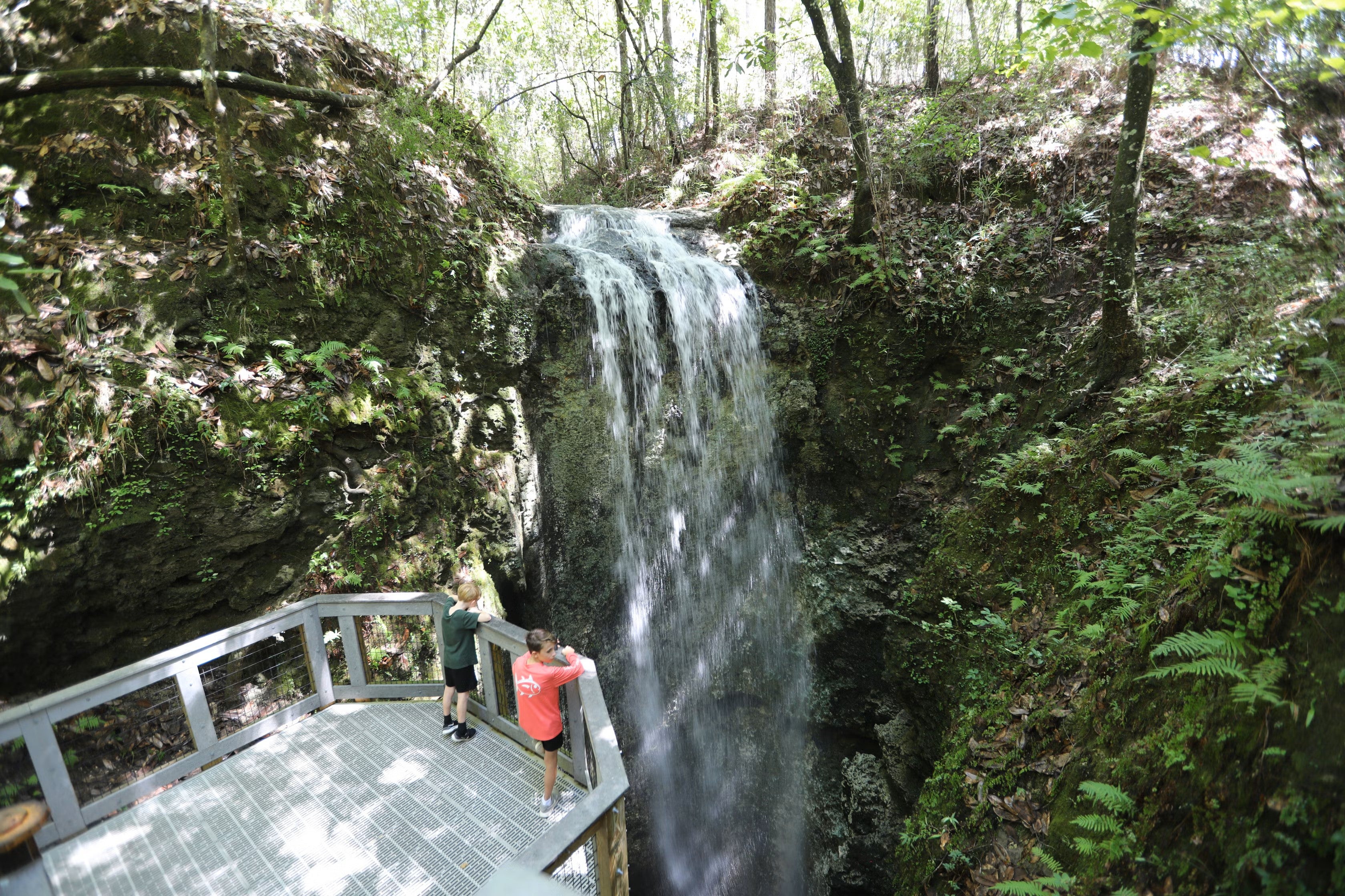 From a viewing deck two boys observe a waterfall as it plunges into a sinkhole.