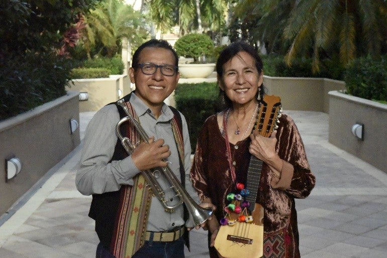 A bespectacled man holding a trumpet posing with a woman holding a charango (a small ukulele shaped instrument). 