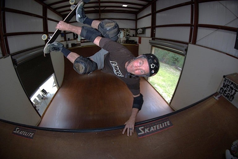 A skateboarder mid-trick with his hand on the rim of a halfpipe and his feet and skateboard in the air above him