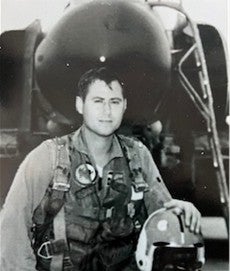 A man wearing a flight suit stands in front of an airplane
