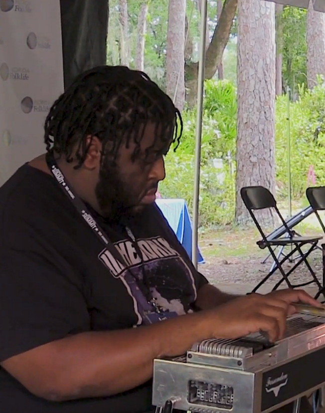 A Black man with braids playing a steel guitar