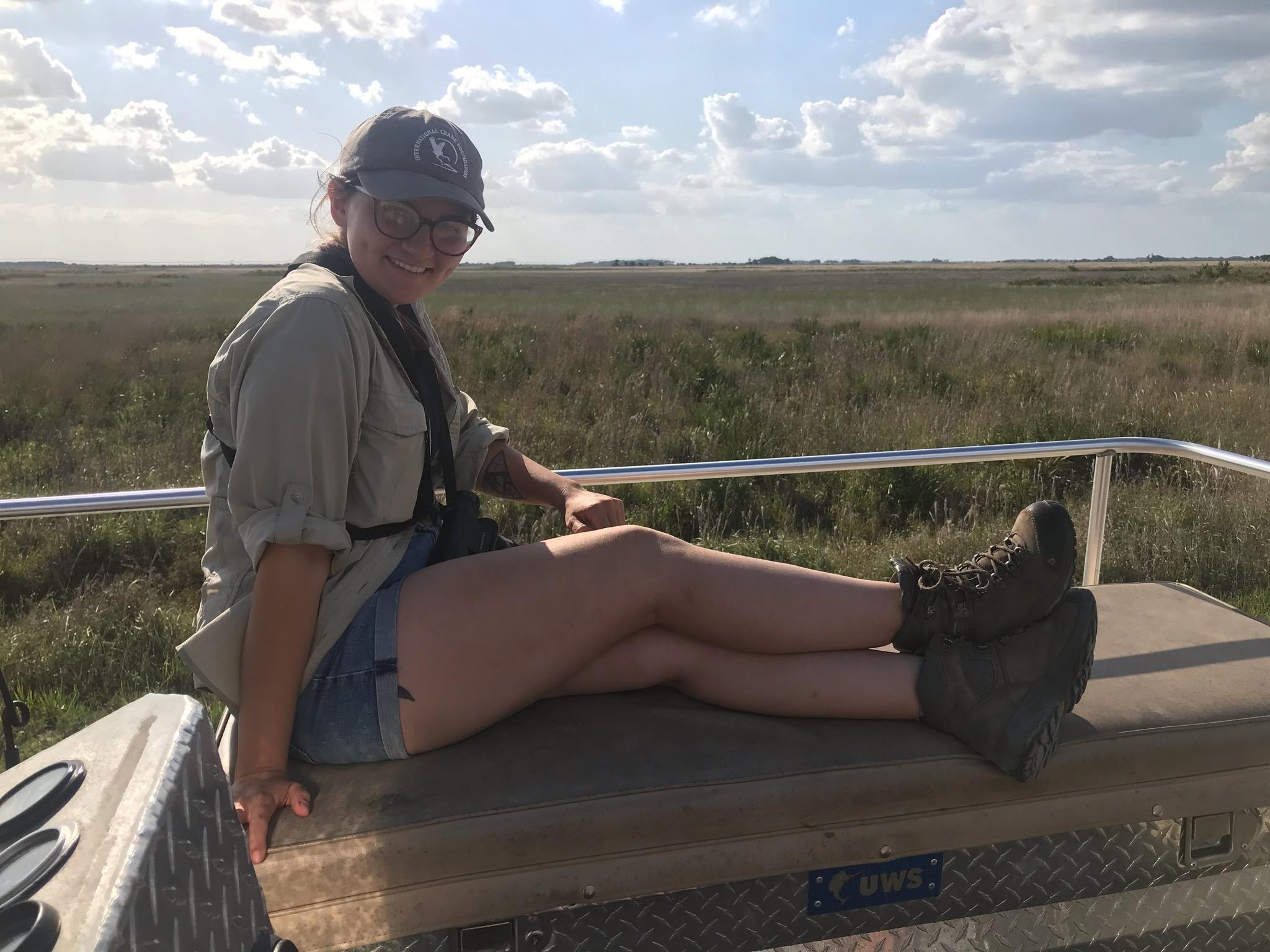 Florida Grasshopper Sparrow Technician Bianca Sicich smiling for the camera with the prairie behind her