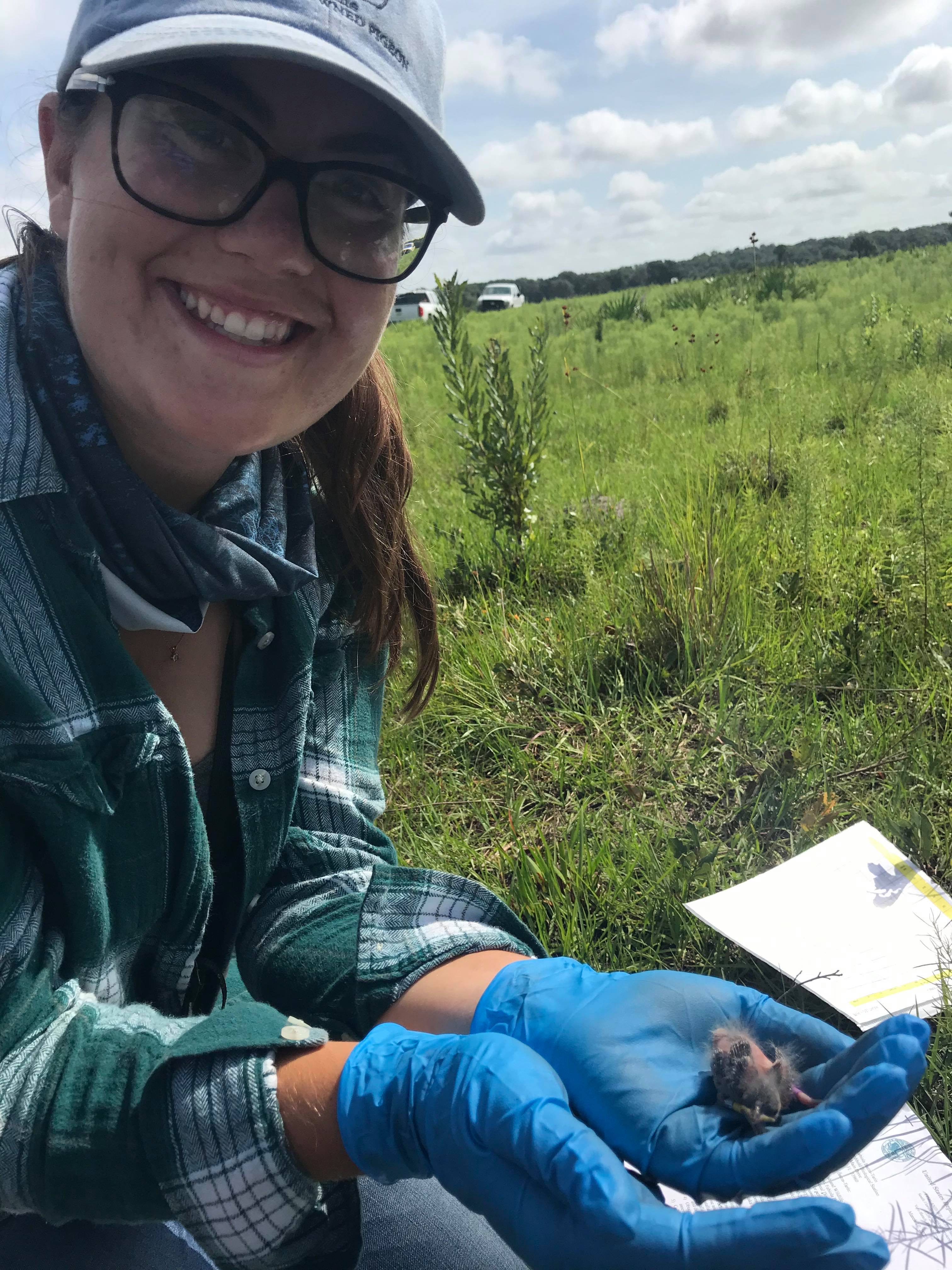 Florida Grasshopper Sparrow Technician Emily Card smiling for the camera and holding a nestling FGSP in her hand