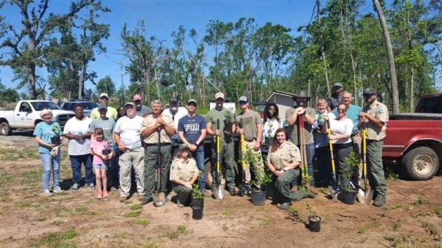 Volunteers, SCC staff group photo at park, posing with shovels and trees in pots. 