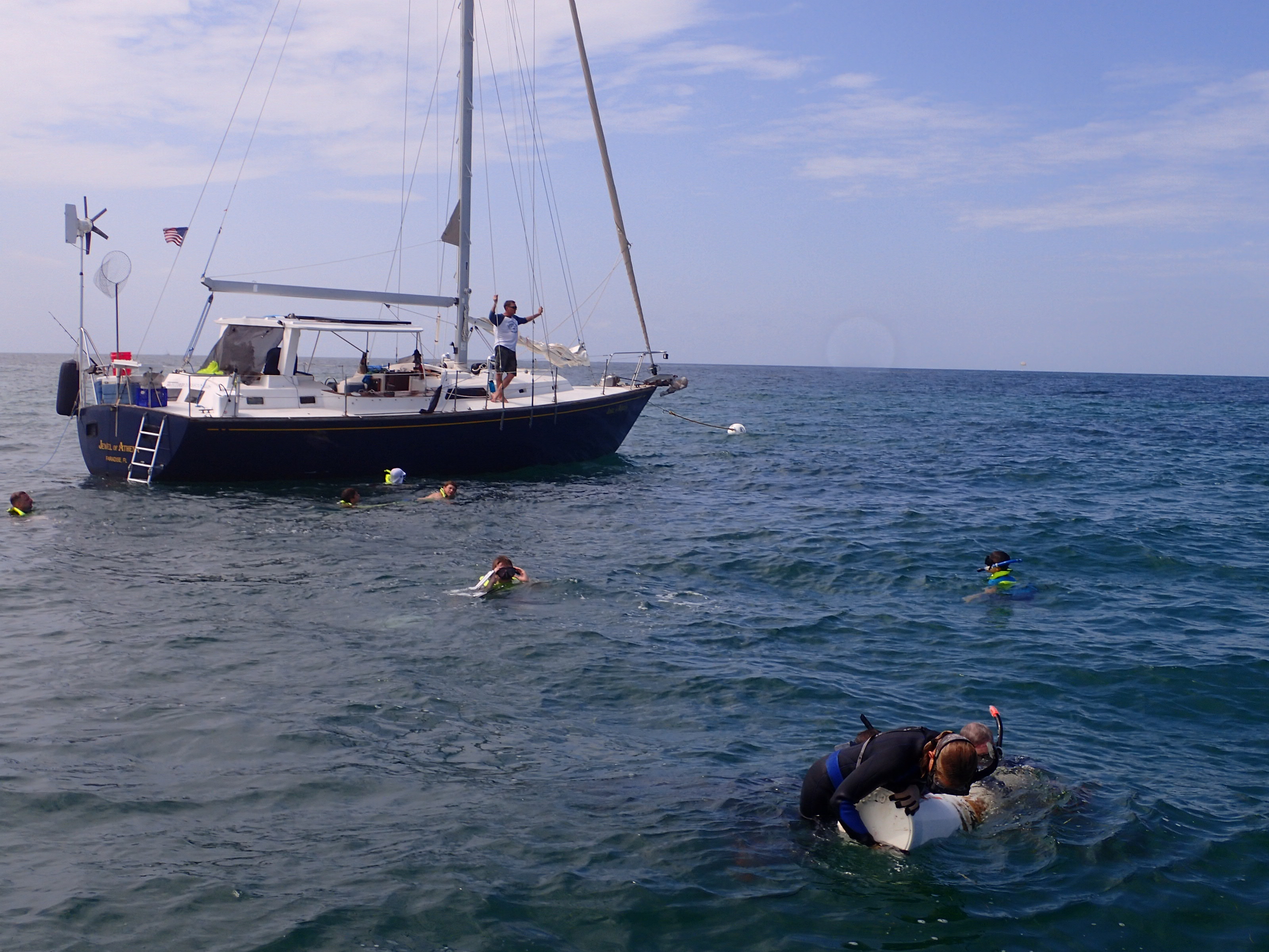 Staff cleaning the informational buoy at San Pedro. A sailboat is tied up to the mooring buoy while a group of Boy Scouts snorkel.