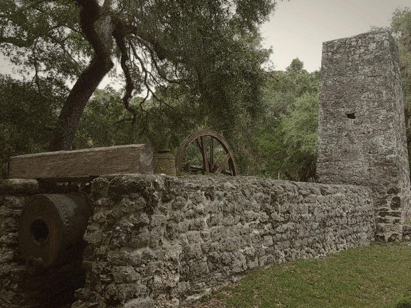 a stone structure with a rusted metal boiler and wheels