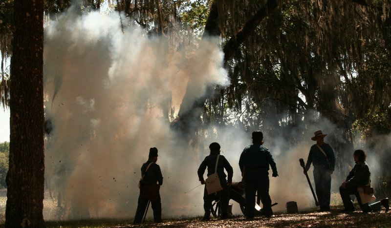 five soldier stand around a just-fired cannon as smoke lifts through the trees.