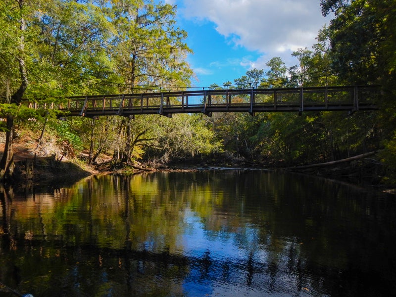 a wooden suspension bridge spans a river covered with green trees