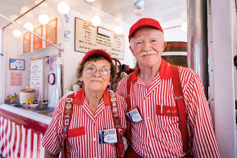 an older man and woman in matching red and white striped outfits stand in front of a food booth smiling