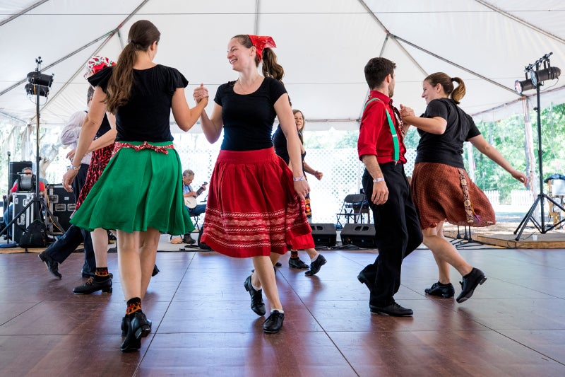 Pairs in bright outfits dance on a wooden stage