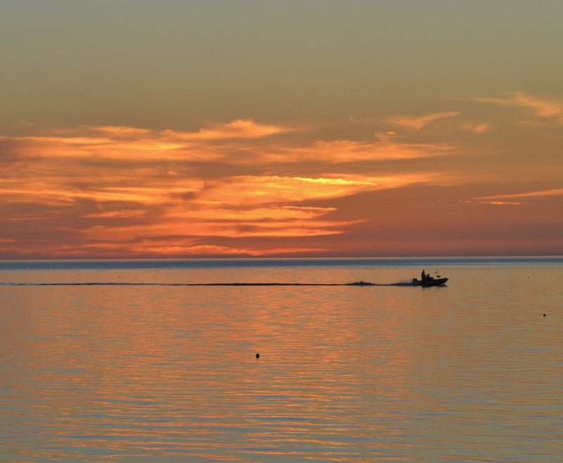 Image of a fishing boat outlined against a beautiful orange sunrise at crystal river preserve state park.