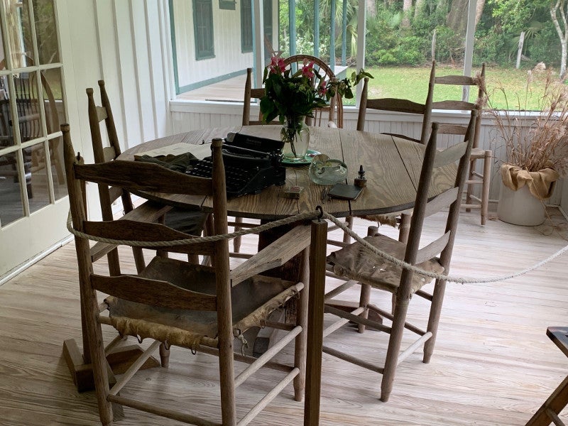 a vase of red flowers and a typewriter sit on a small wooden table with chairs