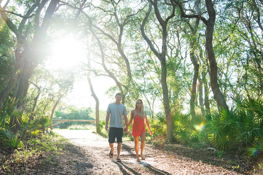 Two people walk hand-in-hand through the trees of the maritime hammock potion of the Dune Ridge Trail