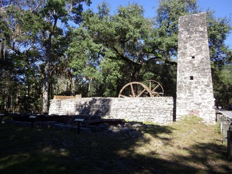 A stone building with a chimney and low walls sits in front of trees