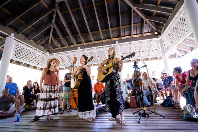 three women sing and play instruments surrounded by a crowd