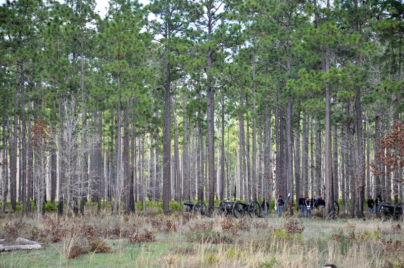 reenactors dressed as union soldiers push a cannon through a thick pine forest