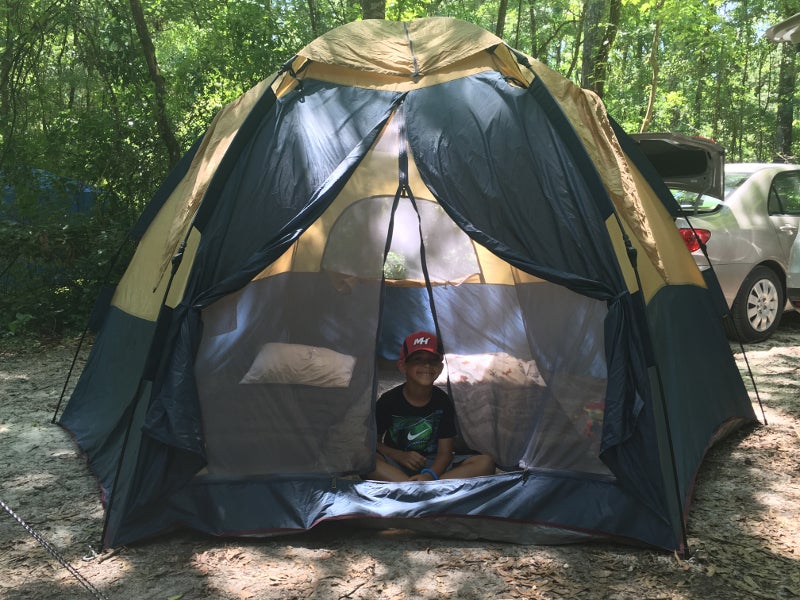 a smiling boy sits in a yellow tent in a campground area