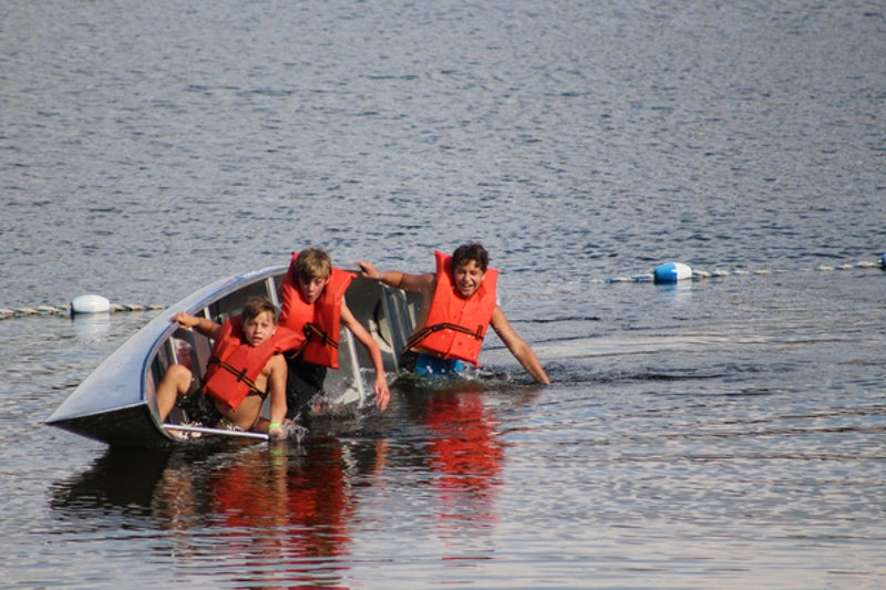 a canoe with three kids wearing bright orange PFD's tips over in the water