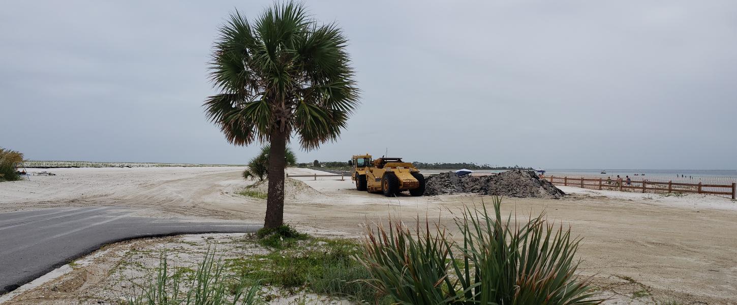 A palm tree stands guard over repairs to the former breach and road.