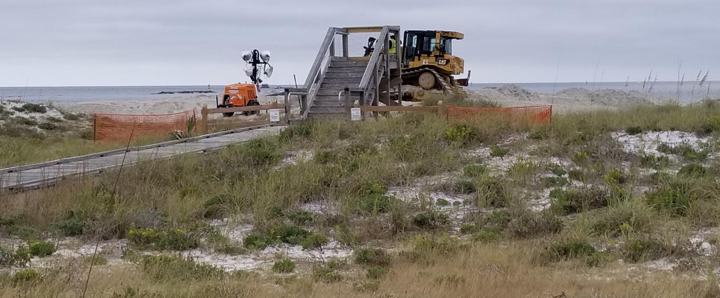 A bulldozer pushes sand on the beach.