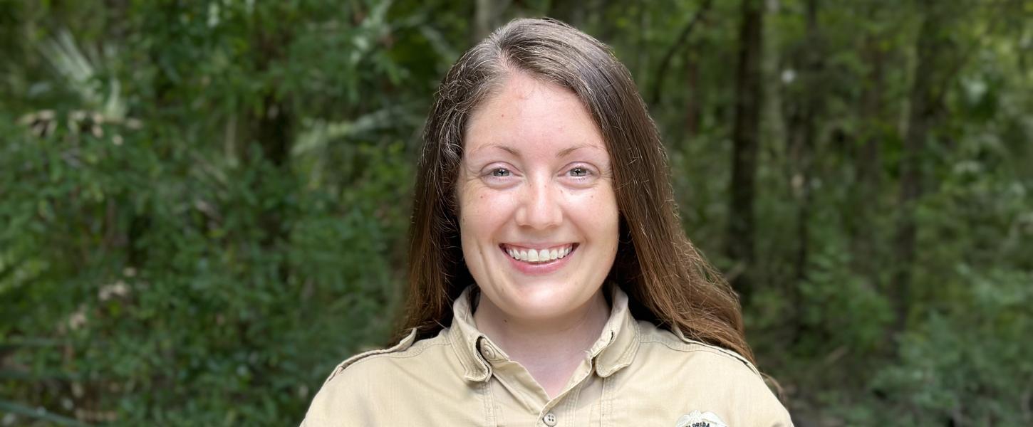 A smiling park ranger standing against a background of forest.