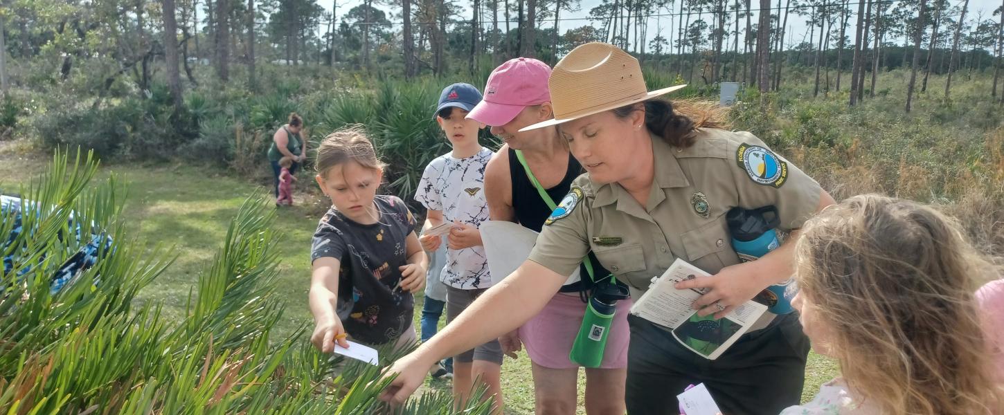 Image of Park Ranger with children observing butterflies in a plant.