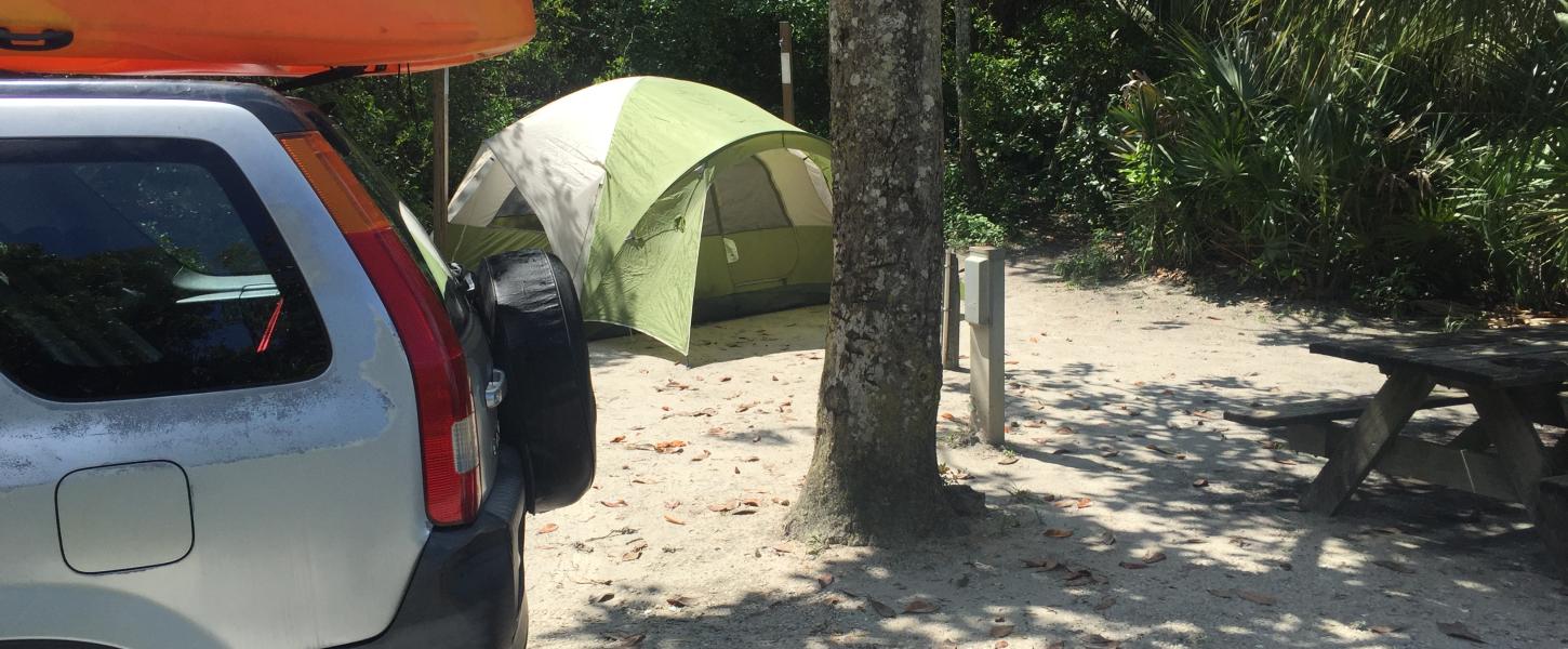 A tent is pitched behind a vehicle with an orange kayak on top.