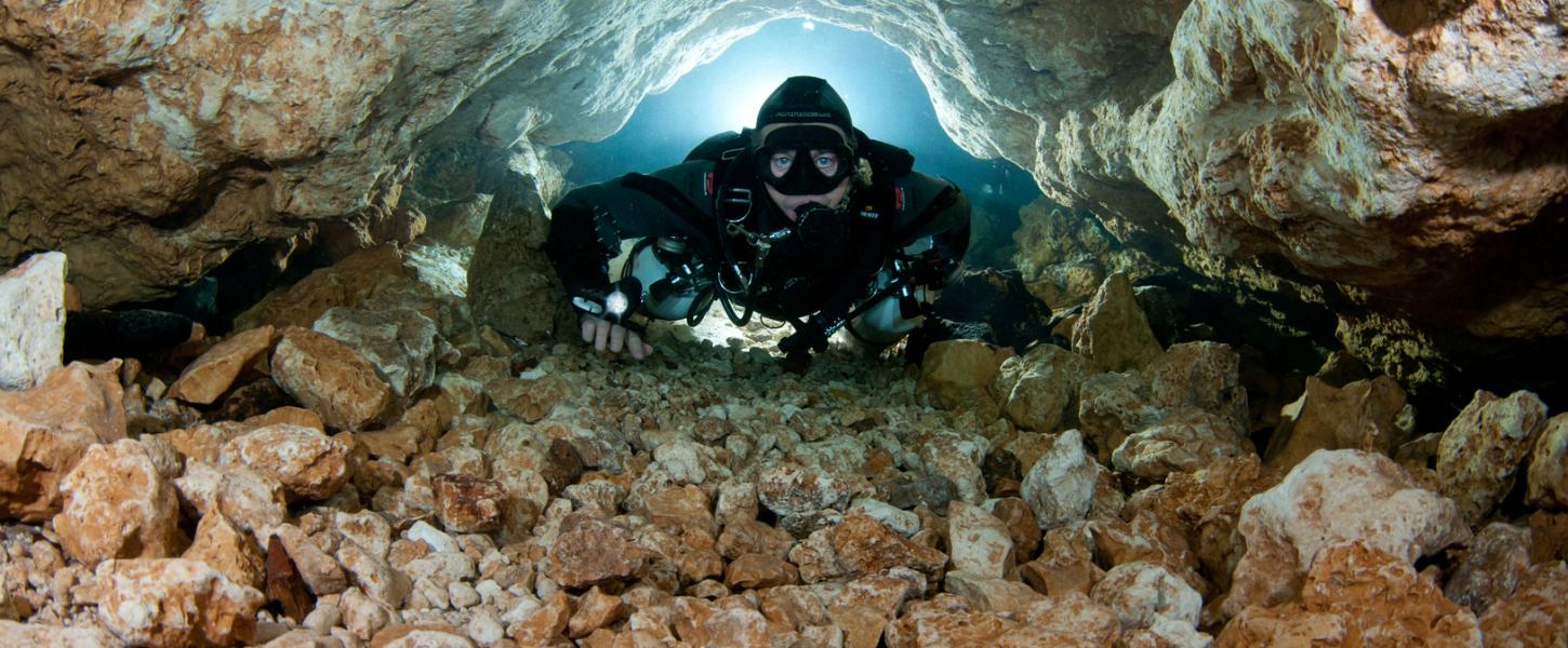 Cave diver navigates narrow stone passage way. 