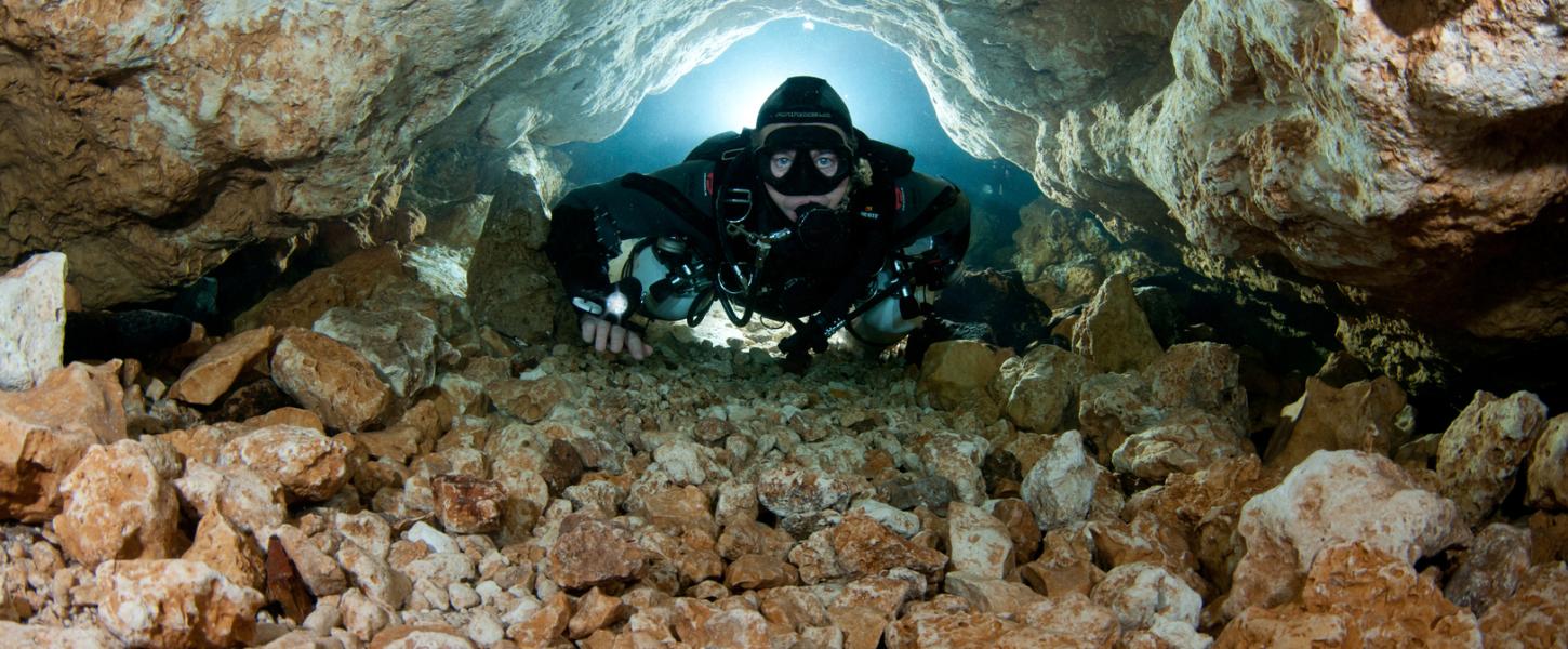 Cave diver navigates narrow stone passage way.