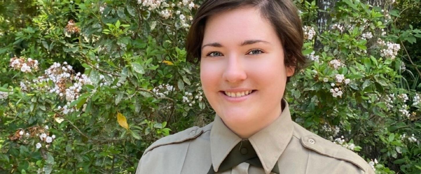 A park ranger in front of a flower bush