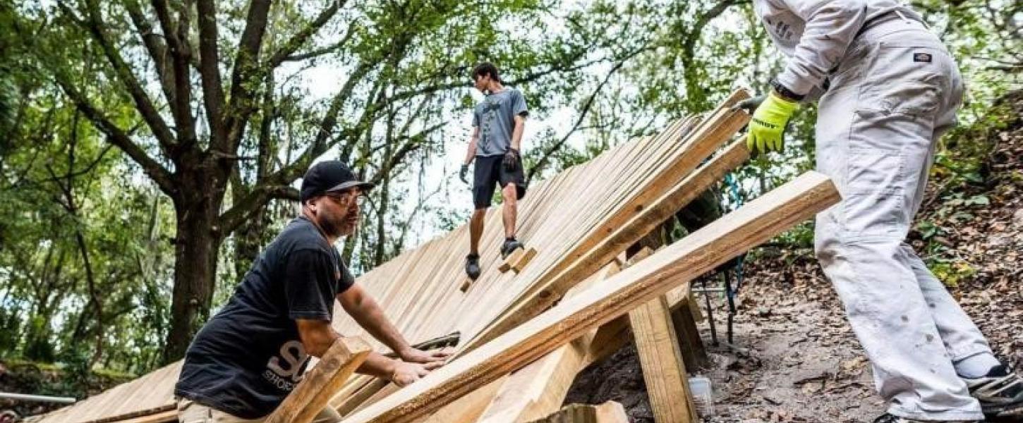 Three people work on a mountain biking trail feature.