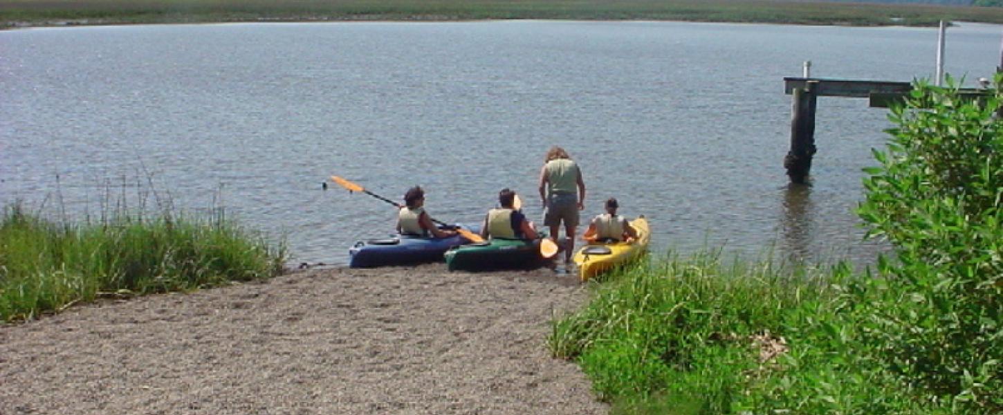 3 kayaks are launched into the water at a sandy ramp.