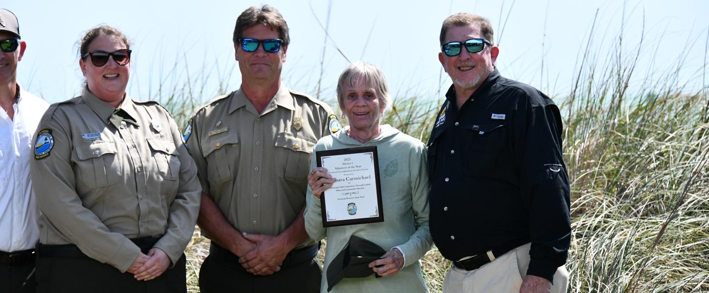volunteer smiling holding award plaque surrounded by park staff