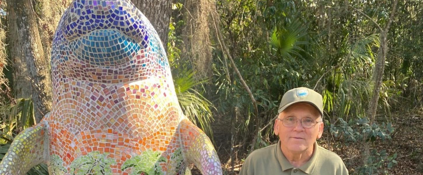 Volunteer Ronnie Coffman poses beside a dolphin statue.