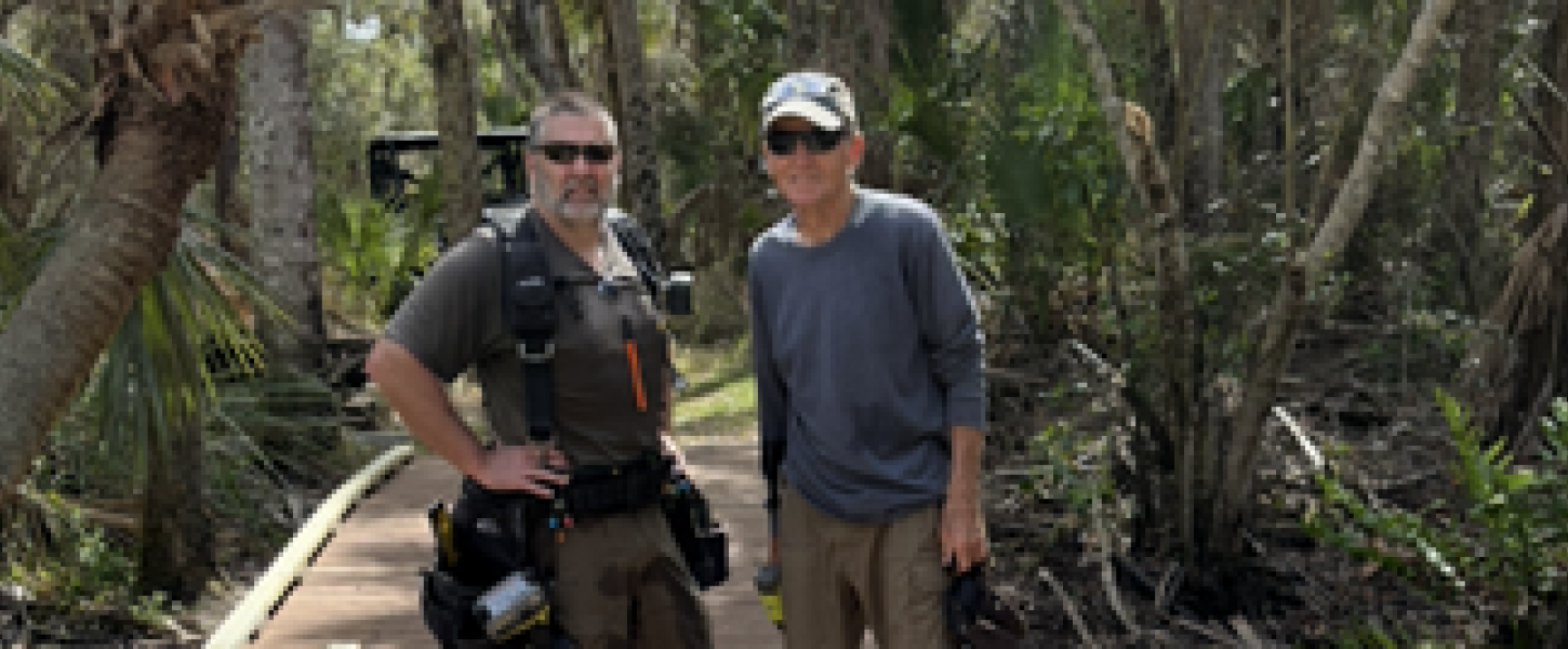 Two men with an assortment of tools standing on a newly-built elevated boardwalk. 
