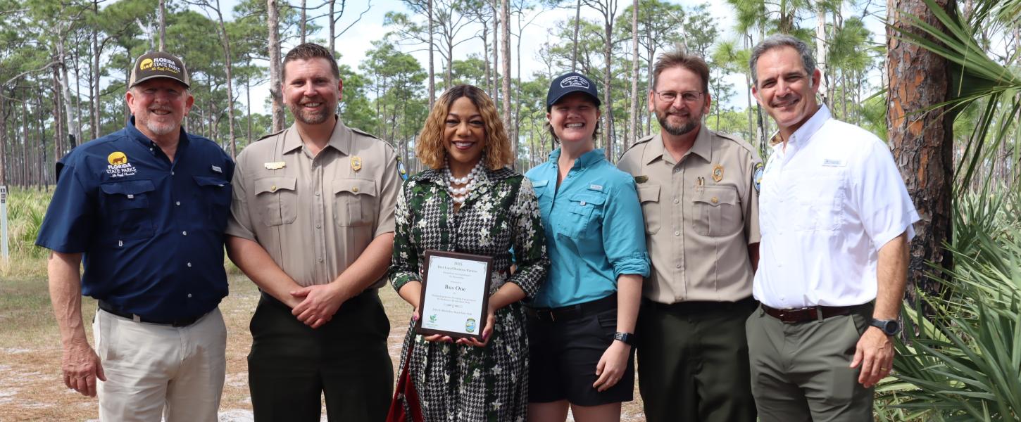 Six people standing shoulder to shoulder. A woman in the middle is holding a plaque