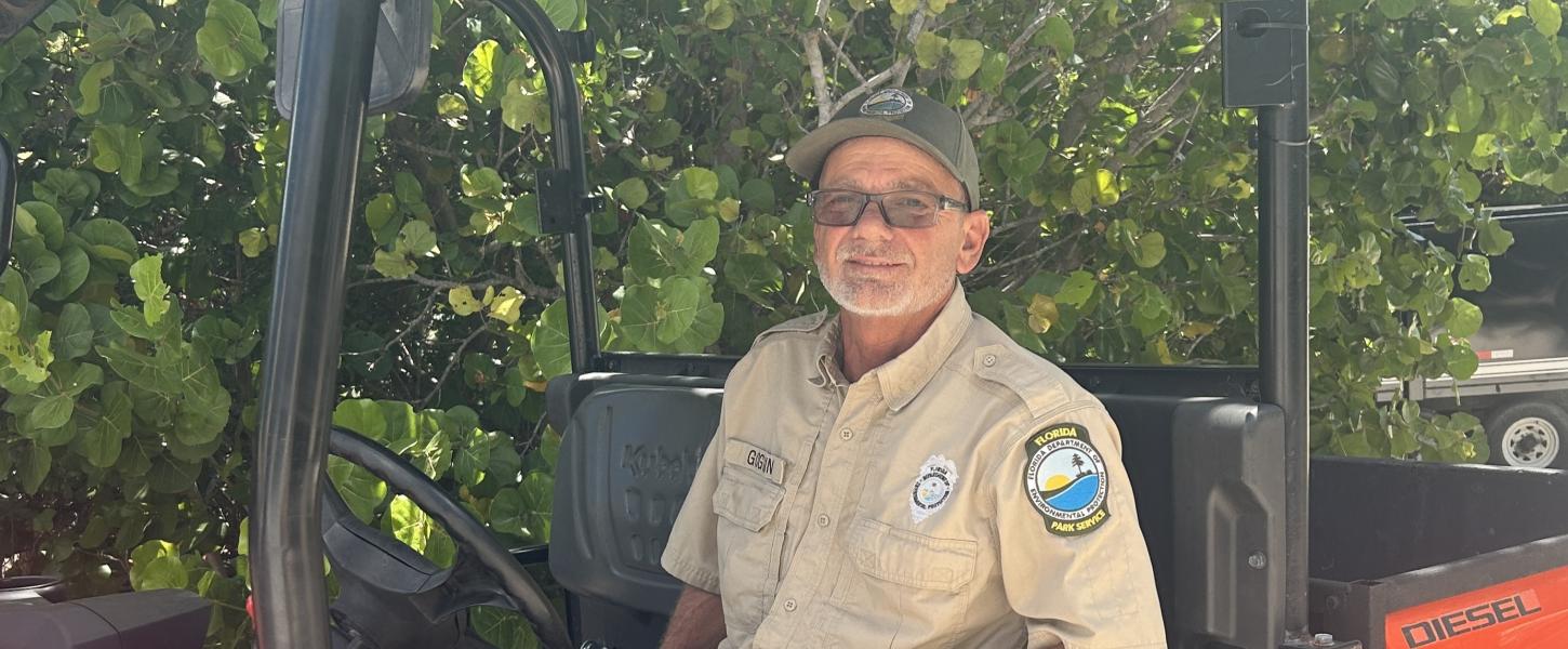 A park ranger in the drivers seat of a UTV, with a background of sea grape plants. 