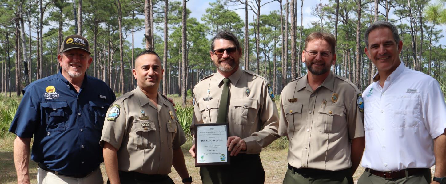 a group of park service staff standing shoulder to shoulder. The park ranger in the middle is holding a plaque. 