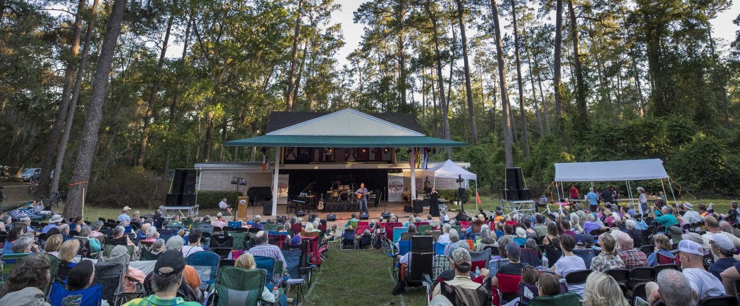 An audience in lawn chairs watching performers on a stage. 
