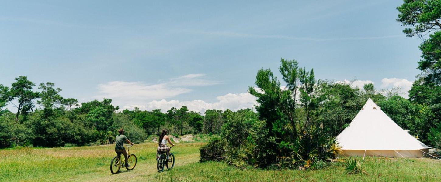 Two people ride bikes towards Fancy Camps tent.