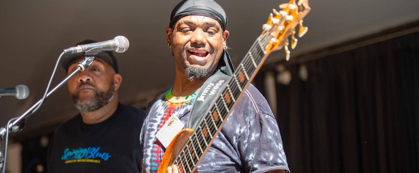 A smiling Black man playing guitar. 