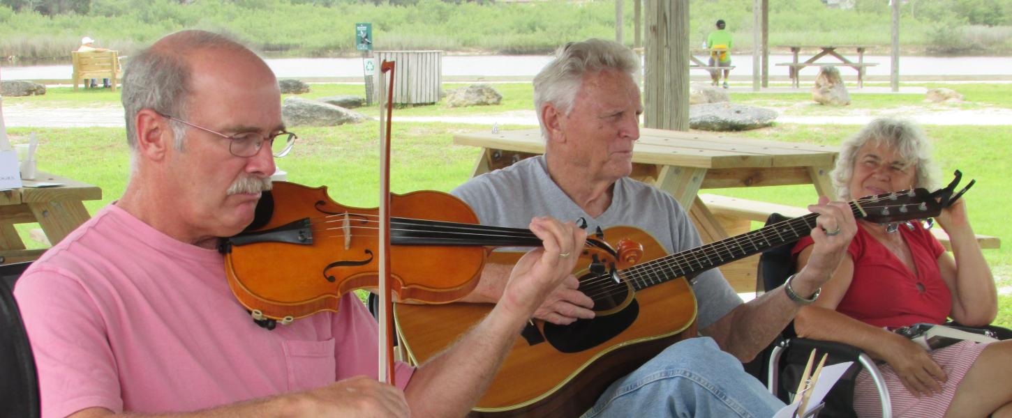 A view of a man playing a violin, and another man playing a guitar, while a woman watches.