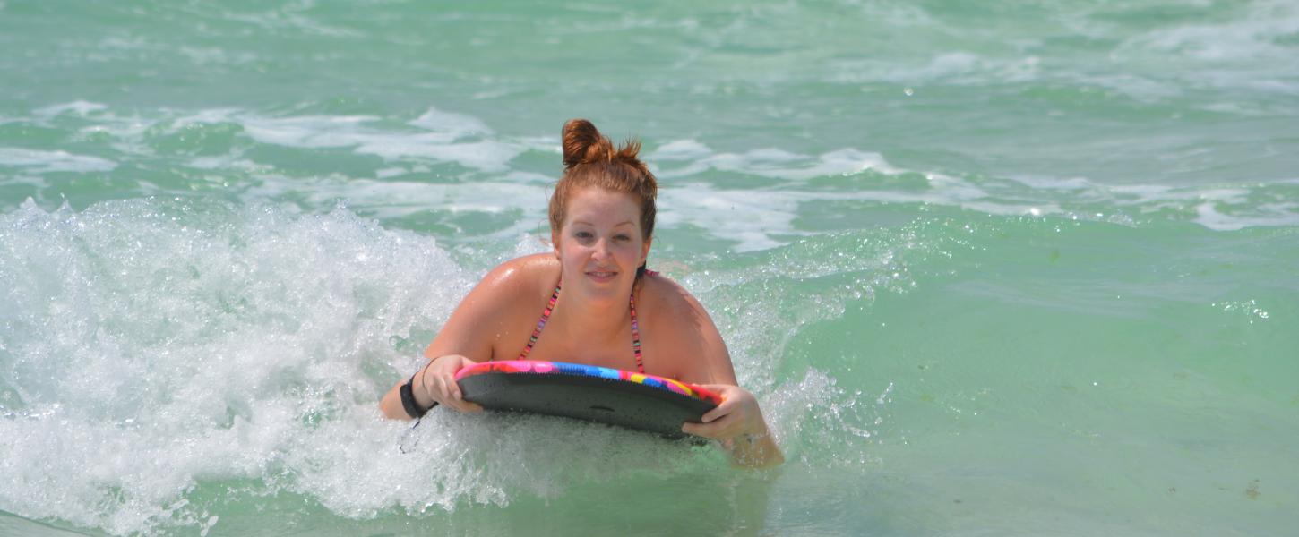 Young girl is all smiles as she glides on wave on her surfboard in emerald green waters. 
