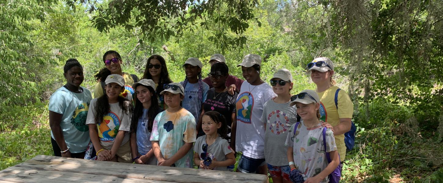 A group of Girl Scouts pose for a photo behind a picnic table.