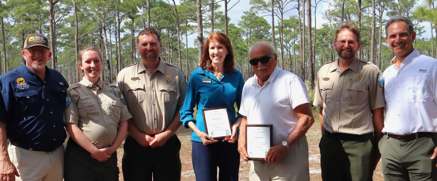 A group of people standing shoulder to shoulder. Two people in the middle are holding plaques. 